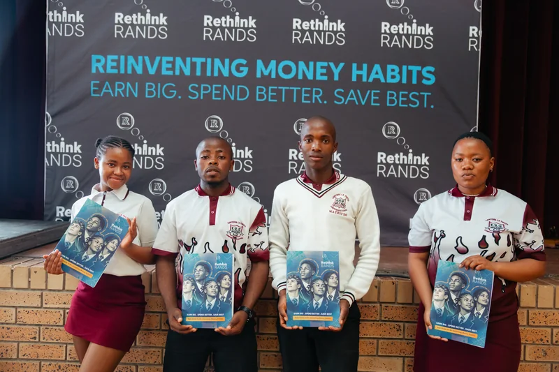 Four learners standing together holding Rethink Rands booklets in front of a branded programme banner.