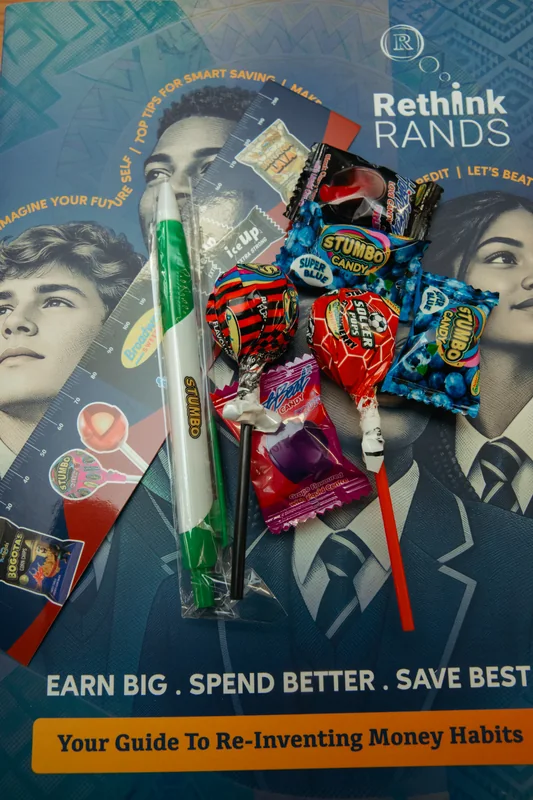 Sweets, a green-and-white pen and rulers arranged on a Rethink Rands financial education booklet.