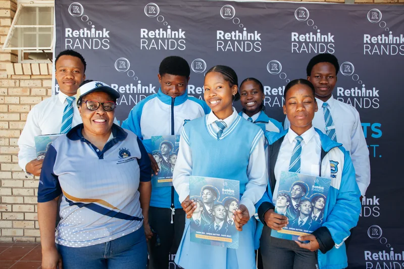 Learners and an adult posing with Rethink Rands booklets in front of a programme banner.