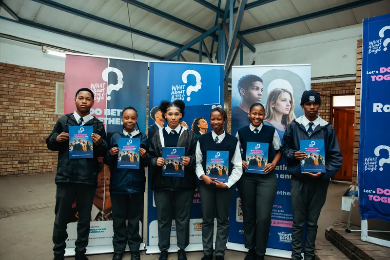 Learners holding What About The Boys booklets in front of branded banners.