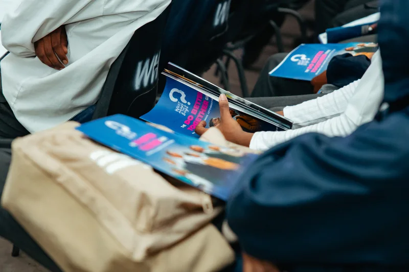 Participants holding What About The Boys programme booklets while seated together.