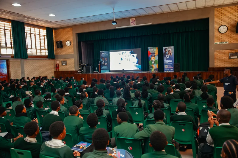 Learners seated in a hall watching a screen beside What About The Boys and Primestars banners.